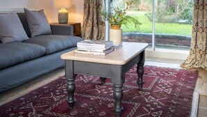 Un salon avec un canapé, une table basse sur laquelle sont posés des livres, une lampe et une vue dégagée sur l’extérieur grâce à une grande fenêtre.