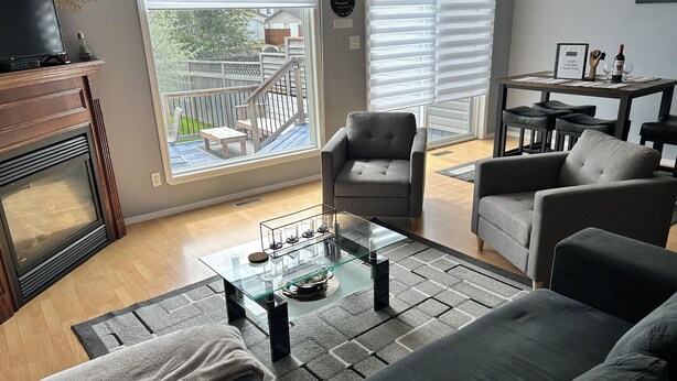 Un salon comprenant un canapé, des fauteuils, une table basse en verre, une cheminée et une vue sur le jardin arrière.