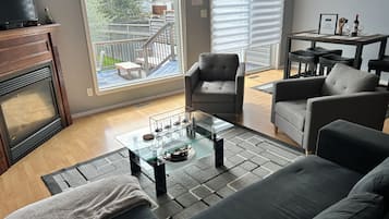 A living room with a sofa, armchairs, a glass coffee table, a fireplace, and a view of the backyard.