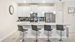 Una cocina moderna con gabinetes blancos, electrodomésticos de acero inoxidable y tres taburetes de bar.