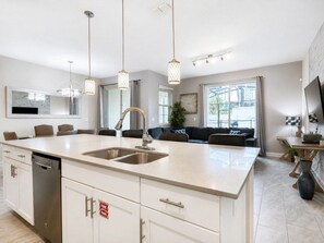 A modern kitchen with a large island, stainless steel appliances, pendant lighting, and a seating area with a sofa and chairs. - 4 Bedrooms / 3 Bathrooms / Storey Lake (4931 WA) (Kissimmee)