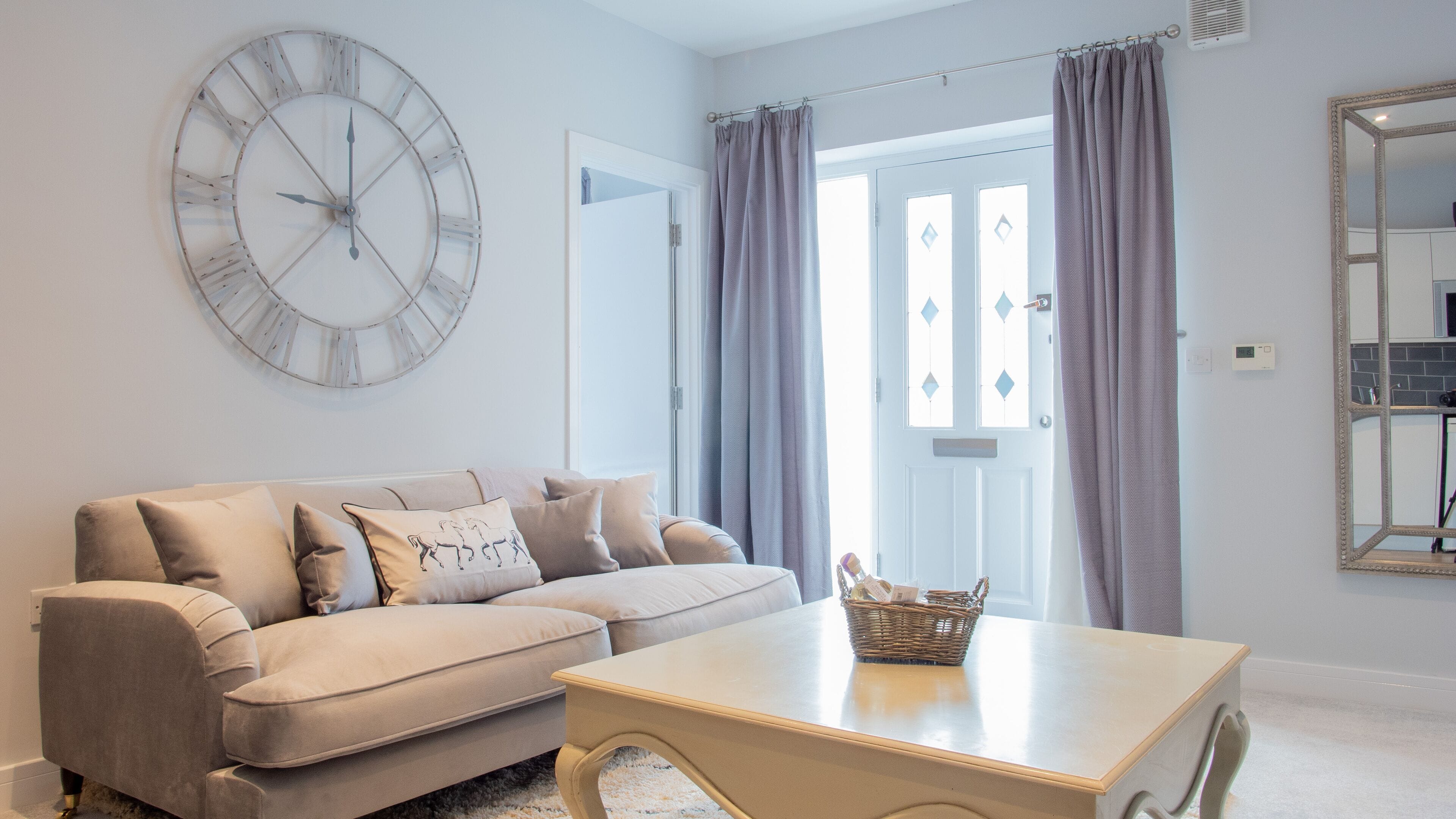 Una sala de estar con un sofá color crema, un reloj de pared redondo, una mesa de centro de madera y un espejo.