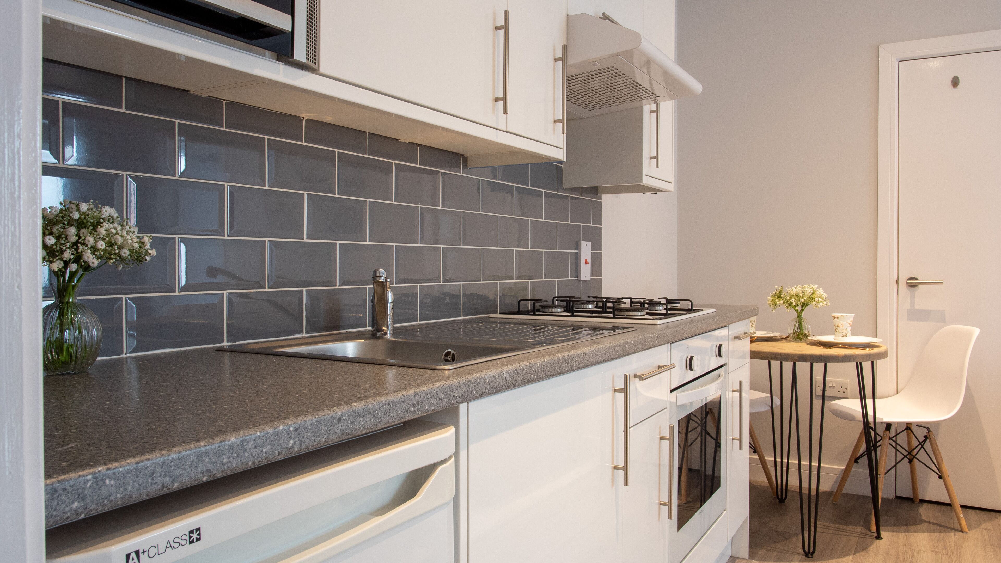 A modern kitchen with grey tiles, stainless steel appliances, and white cabinetry.