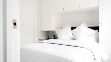 Un lit bien fait, avec une literie blanche, une table de chevet avec une lampe et un meuble fixé au mur.