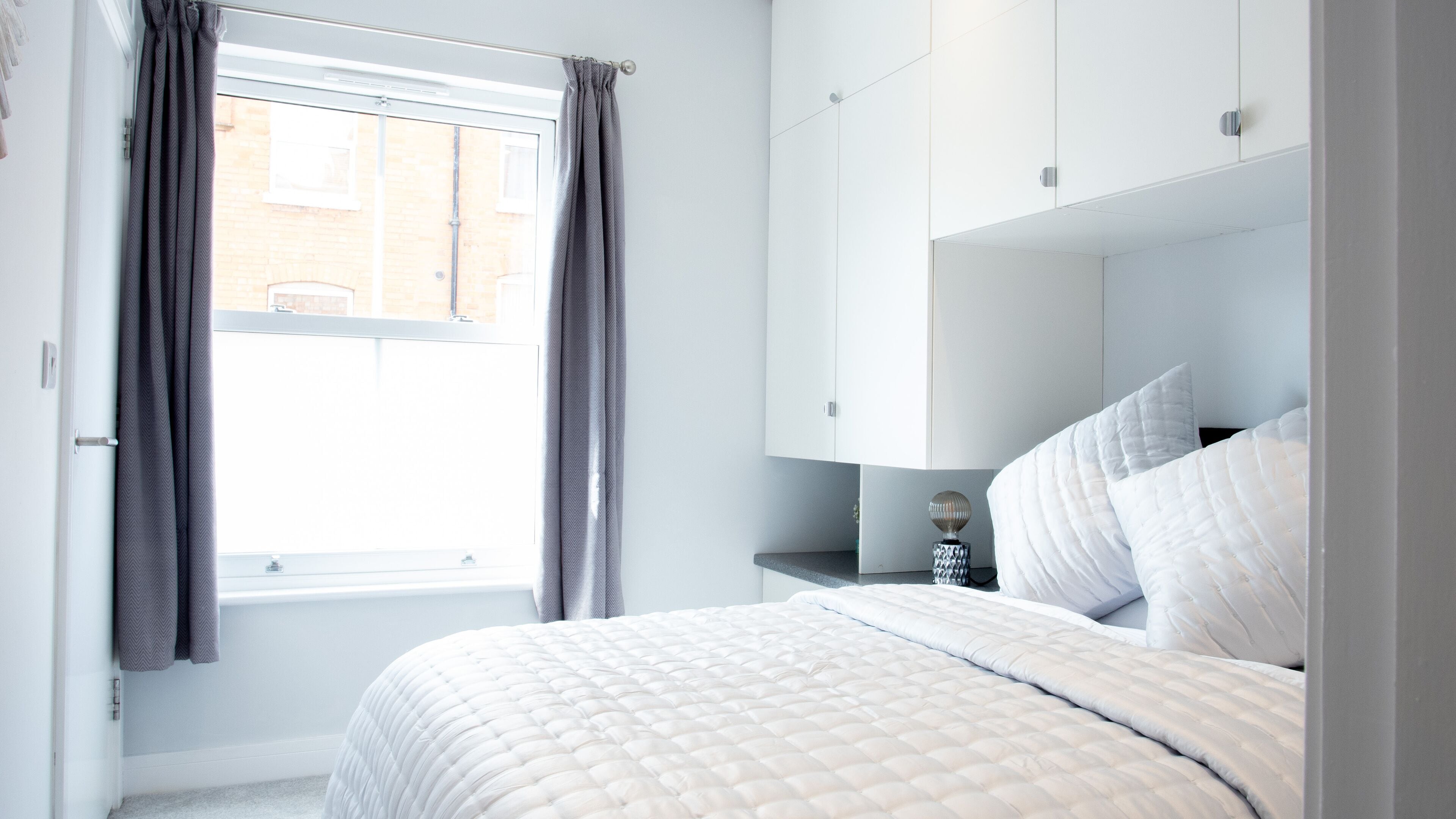 A bedroom with a bed, a nightstand, a mirror, and a window with curtains.