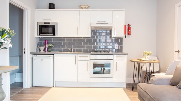 A compact kitchen with white cabinetry, a built-in microwave, a stove, and a dishwasher. - Modern Apartment in Stratford Upon Avon With Parking Wifi and Netflix (Stratford-upon-Avon)