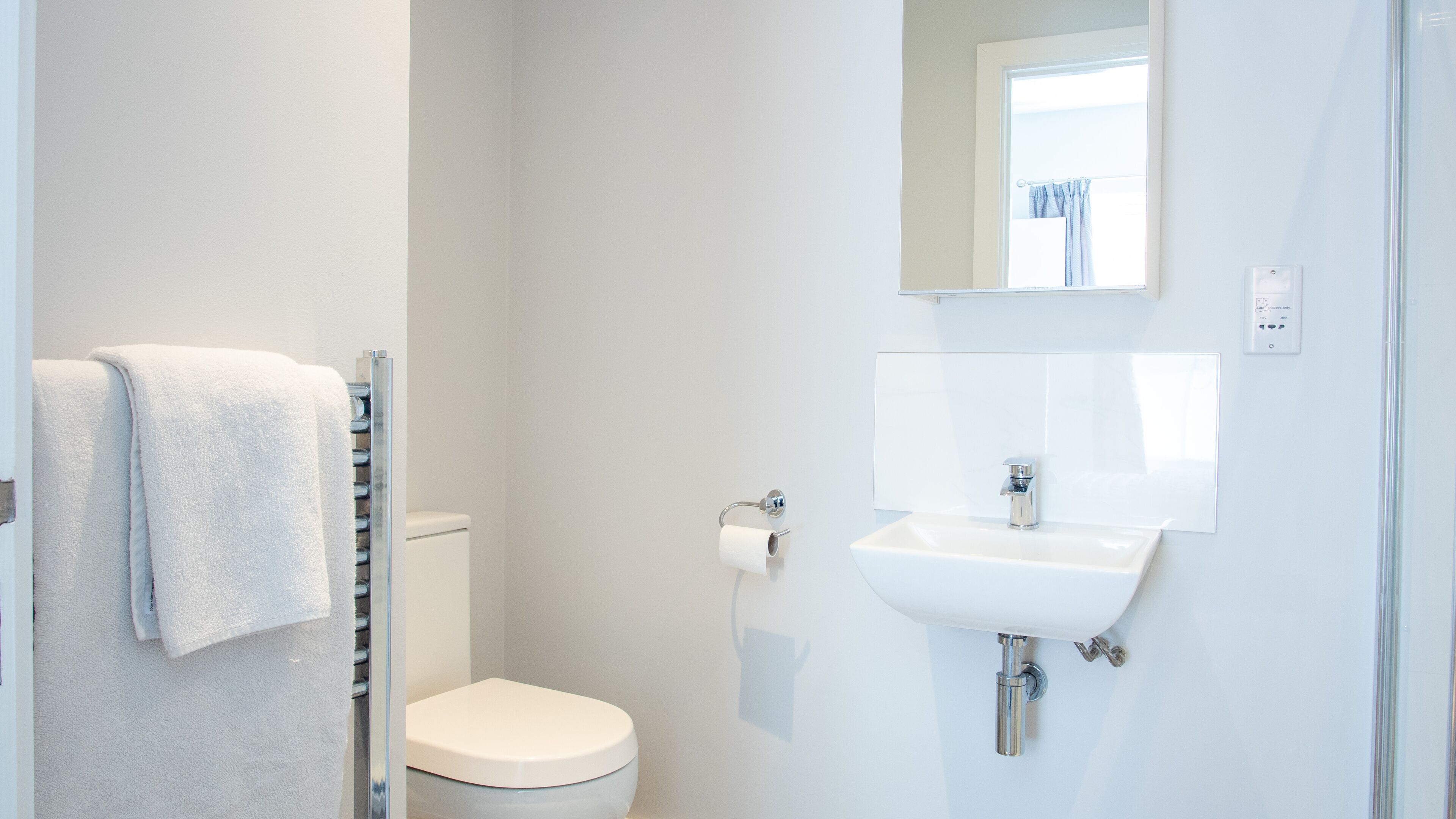 Een badkamer met toilet, wastafel, handdoekhouder en spiegel.