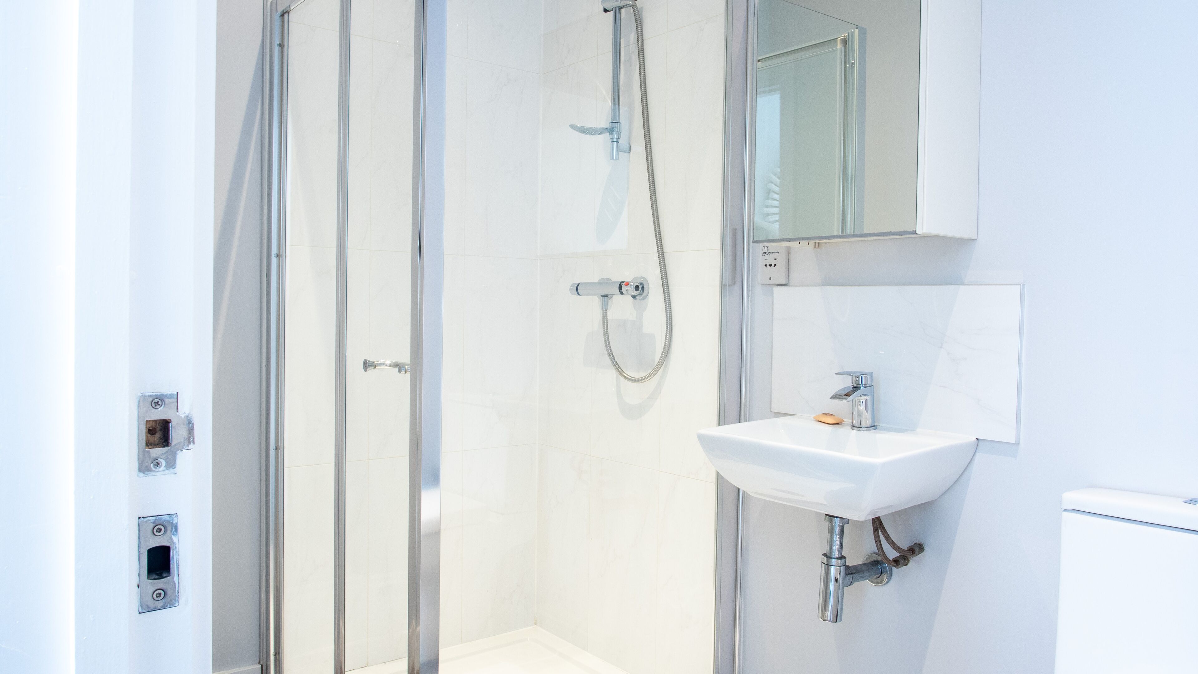 Un baño moderno con cabina de ducha de vidrio, un lavabo blanco y un espejo sobre el lavabo.