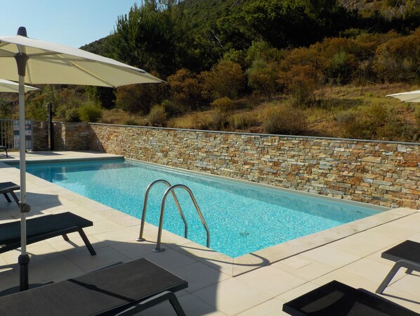 Piscina com paredes de pedra, escada de metal e espreguiçadeiras.