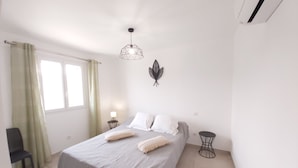 Un dormitorio con cama, escritorio, silla, ventana con cortinas y una lámpara de pared.
