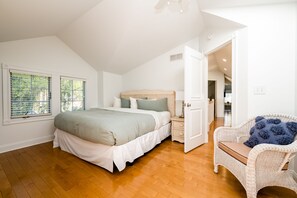 Ein Schlafzimmer mit einem großen Bett, einem Korbstuhl und Blick in die Küche durch eine offene Tür.