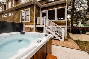 A hot tub in front of a house with a covered porch and a staircase.