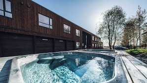Un bâtiment moderne avec un revêtement mural en bois et une terrasse en bois équipée de deux bains à remous.