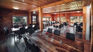 Un vaste espace de salle à manger en bois, doté de plusieurs tables et chaises, de grandes fenêtres et offrant une vue sur l’extérieur.