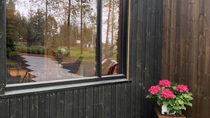 Un intérieur moderne avec une grande fenêtre qui reflète un jardin et des arbres. On y trouve une petite table en bois sur laquelle est posée une plante en pot.