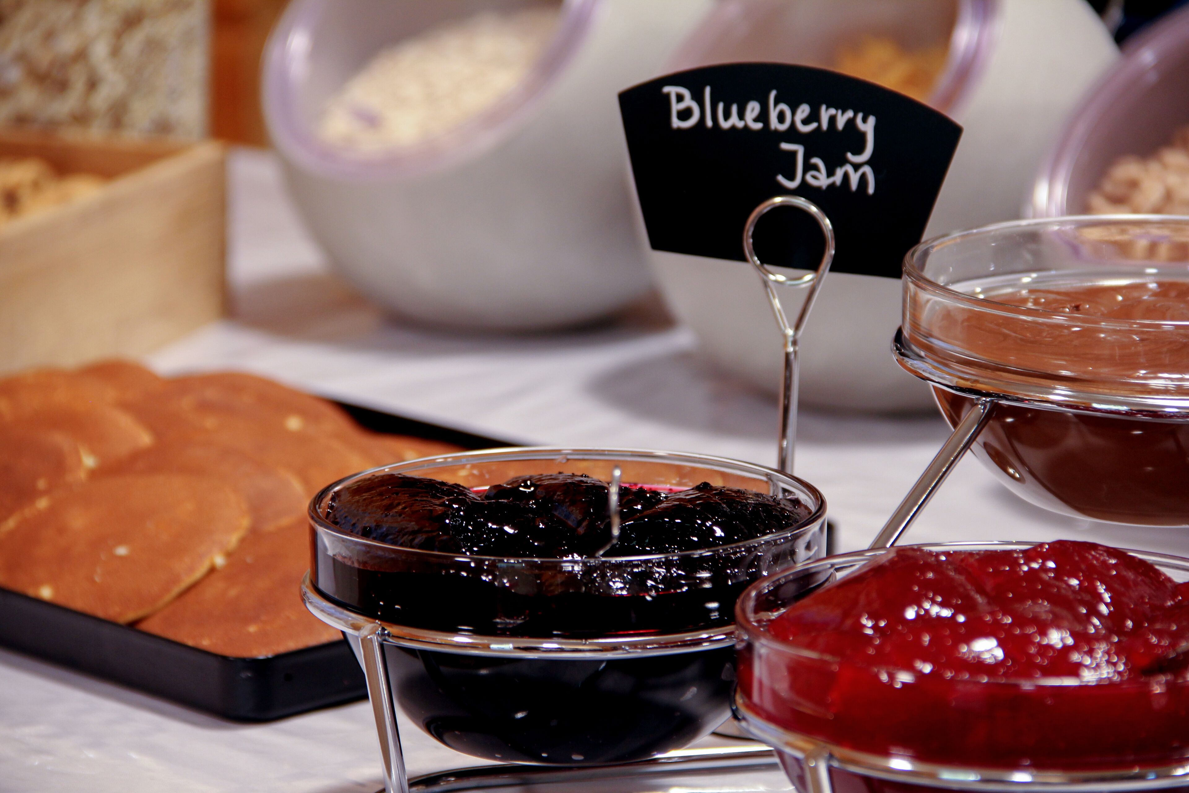 Une table sur laquelle on trouve divers aliments, notamment une assiette de crêpes, un bol de confiture de myrtilles et un bol de confiture rouge.