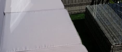 Un conjunt de seients de vimetra amb coixins gris, disposats a l'exterior.