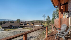 A wooden deck with a chair, overlooking a parking area and buildings with multiple roofs. - Dog Friendly Luxury Townhome on Golf Course (Bigfork)