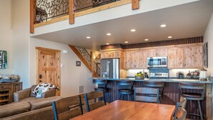 A spacious kitchen with wooden cabinets, a stainless steel refrigerator, and a microwave. There is a dining area with a wooden table and chairs. - Dog Friendly Luxury Townhome on Golf Course (Bigfork)