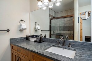 Un baño moderno con encimera de mármol, lavamanos y un espejo grande.