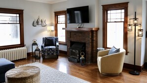 Un salon avec une cheminée, un téléviseur fixé au-dessus, deux fauteuils, une lampe sur pied et un radiateur.