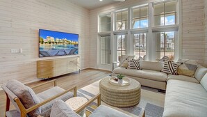 A spacious living room with a large TV, comfortable seating, and large windows offering a view of the outside.