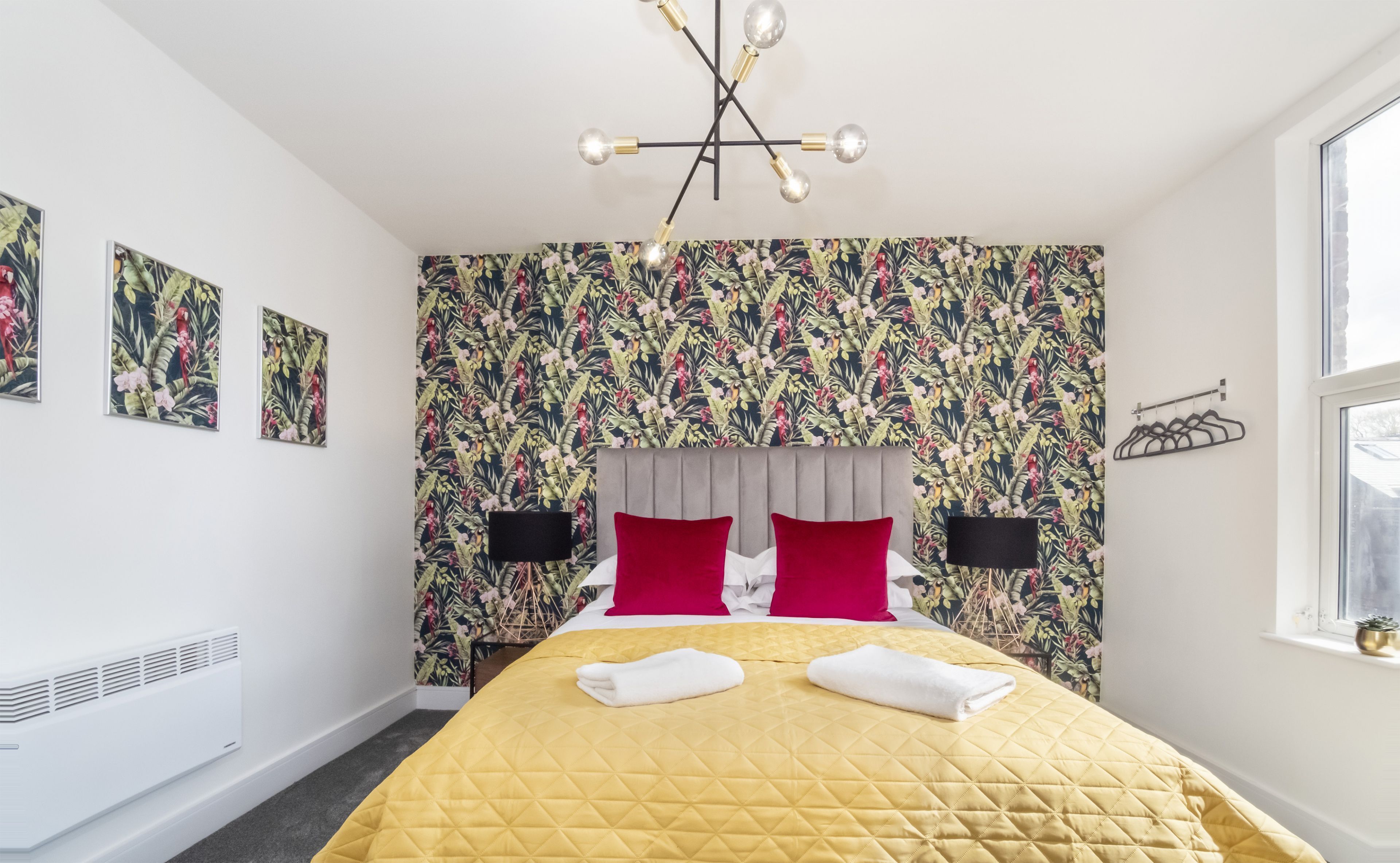 A hotel room with a bed, a radiator, a window, and a wall with floral wallpaper.
