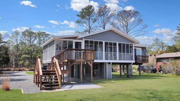 A two-story house with a balcony and a wooden staircase. - Our Happy Place | Canal Front w/ Private Dock, Huge Screened Porch + Pet Friendly Escape (Chincoteague Island)