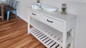 A white vanity with a mirror, a plant, and a small jar on the countertop. - Our Happy Place | Canal Front w/ Private Dock, Huge Screened Porch + Pet Friendly Escape (Chincoteague Island)