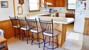 A kitchen with wooden cabinets, a central island with bar stools, a refrigerator, and a microwave. - Charming, well maintained contemporary home with every attention to detail. (Duck)