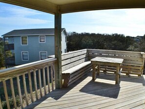 Une terrasse en bois avec un banc et une table, donnant sur un quartier résidentiel avec des maisons et des arbres.