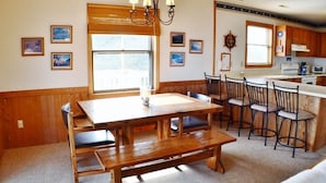 A dining area with a wooden table and benches, a chandelier, and framed pictures on the walls. - Charming, well maintained contemporary home with every attention to detail. (Duck)