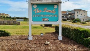 A sign for "The Sands Condominiums" with a clear view of the surrounding area including houses and a grassy field. - Oceanfront Condo on the Outer Banks (Kill Devil Hills)
