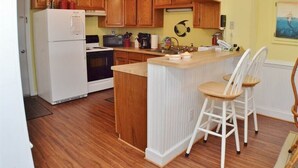 A kitchen with wooden cabinets, a white refrigerator, a built-in island with bar stools, and a ceiling fan. - Oceanfront Condo on the Outer Banks (Kill Devil Hills)