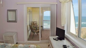 A room with a bed, a desk, a chair, a TV, and a view of the ocean. - Oceanfront Condo on the Outer Banks (Kill Devil Hills)
