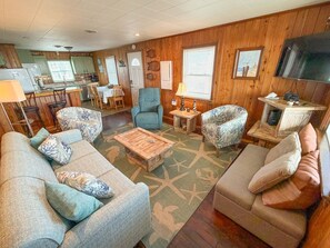 A cozy living room with a sofa, armchairs, a coffee table, and a TV. - Charming Oceanfront retreat (Kill Devil Hills)
