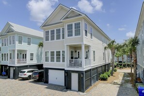 A multi-story residential building with a balcony on the second floor, a garage, and a paved driveway.