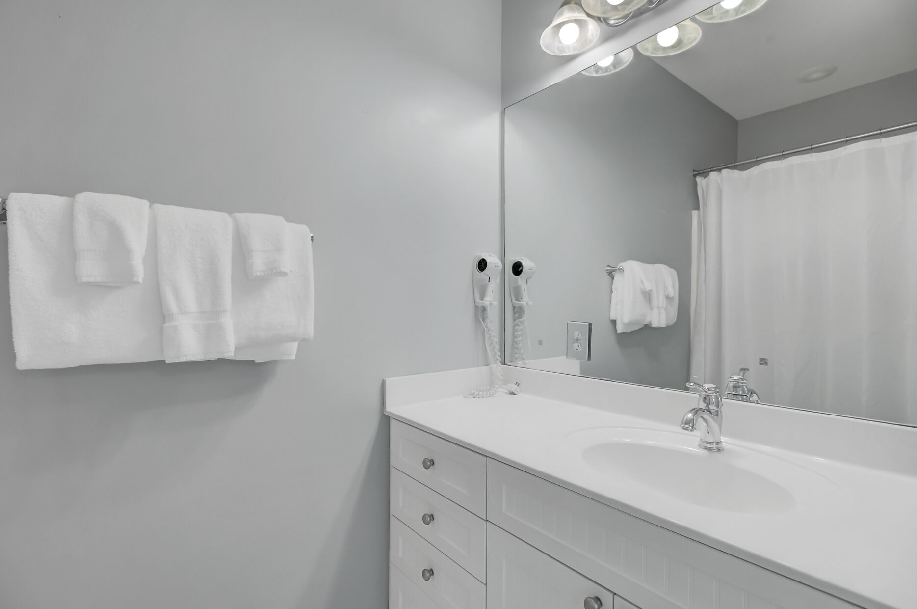 Une salle de bain moderne avec un grand miroir, un lavabo blanc et un porte-serviettes.