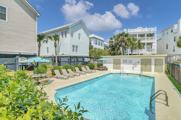 A swimming pool with lounge chairs and umbrellas, surrounded by buildings with balconies and a sign indicating no lifeguard on duty.