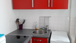 Eine kompakte Küche mit roten Schränken, einer Edelstahl-Spüle, einem weißen Kühlschrank und einem eingebauten Backofen.