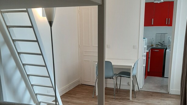 Ein großzügiger Wohnbereich mit modernem Design, inklusive eines weißen Sofas, eines runden Tisches und einer Stehlampe. Eine Treppe führt auf eine obere Ebene, und im Hintergrund ist eine Küchenzeile zu sehen.