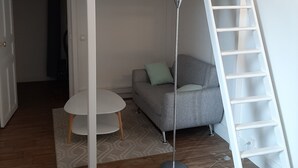 Ein Zimmer mit einem Etagenbett, einem runden Tisch, einer Couch und einer Leiter.