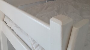 Ein Einzelbett mit weißem Kopfteil und Fußteil, ein kleines Fenster und eine Tür im Zimmer.