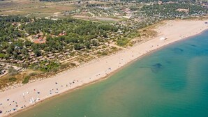 An aerial view of a coastal area with a sandy beach, a small town with houses, and a clear view of the sea. - Loue Mobilhome (Sérignan)