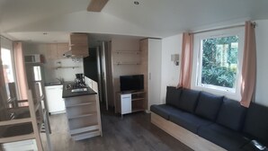 A compact living space with a kitchenette, a sofa, and a TV. - Loue Mobilhome (Sérignan)