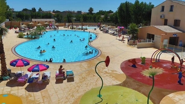 A large outdoor swimming pool surrounded by lounge chairs and umbrellas, with a water play area nearby. - Loue Mobilhome (Sérignan)