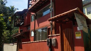 Un edificio rojo de dos pisos con un balcón, una puerta de madera y un letrero que indica servicio de seguridad las 24 horas.