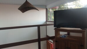Una habitación con un mueble bajo de televisión de madera, un ventilador de techo y una ventana con vistas a árboles.