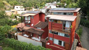 Un edificio de varios pisos con paneles solares en el techo, rodeado de exuberante vegetación y otras edificaciones residenciales.
