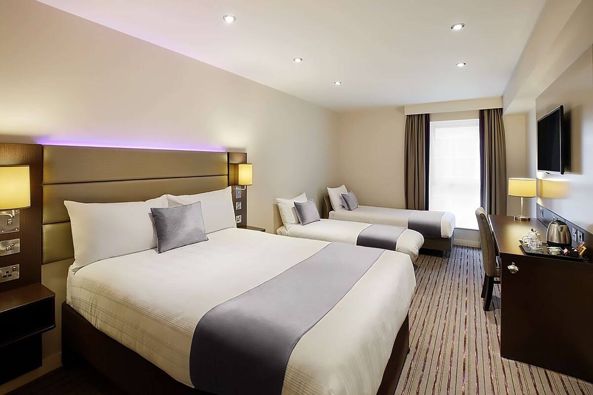 A hotel room with a large bed, a smaller bed, a desk with a TV, and a window with curtains.